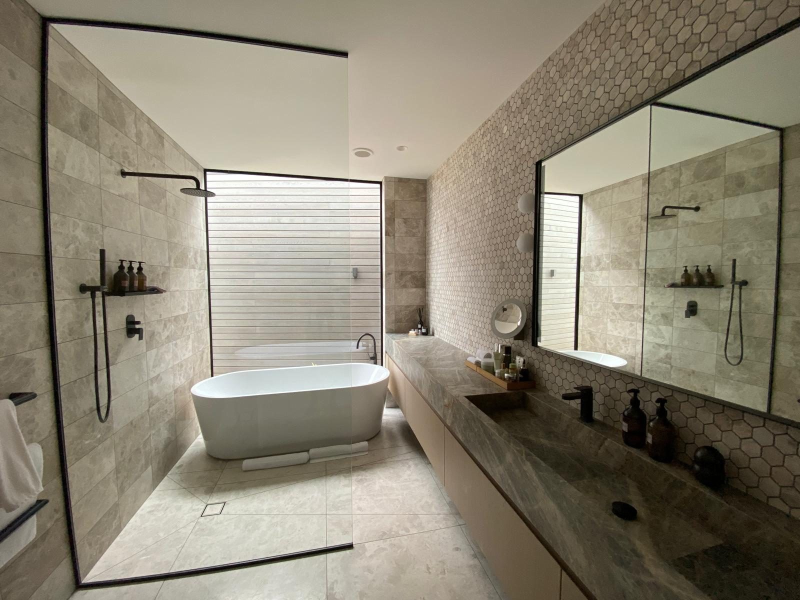 Finished bathroom — stone vanity, hexagon mosaic wall, freestanding bath and walk-in shower