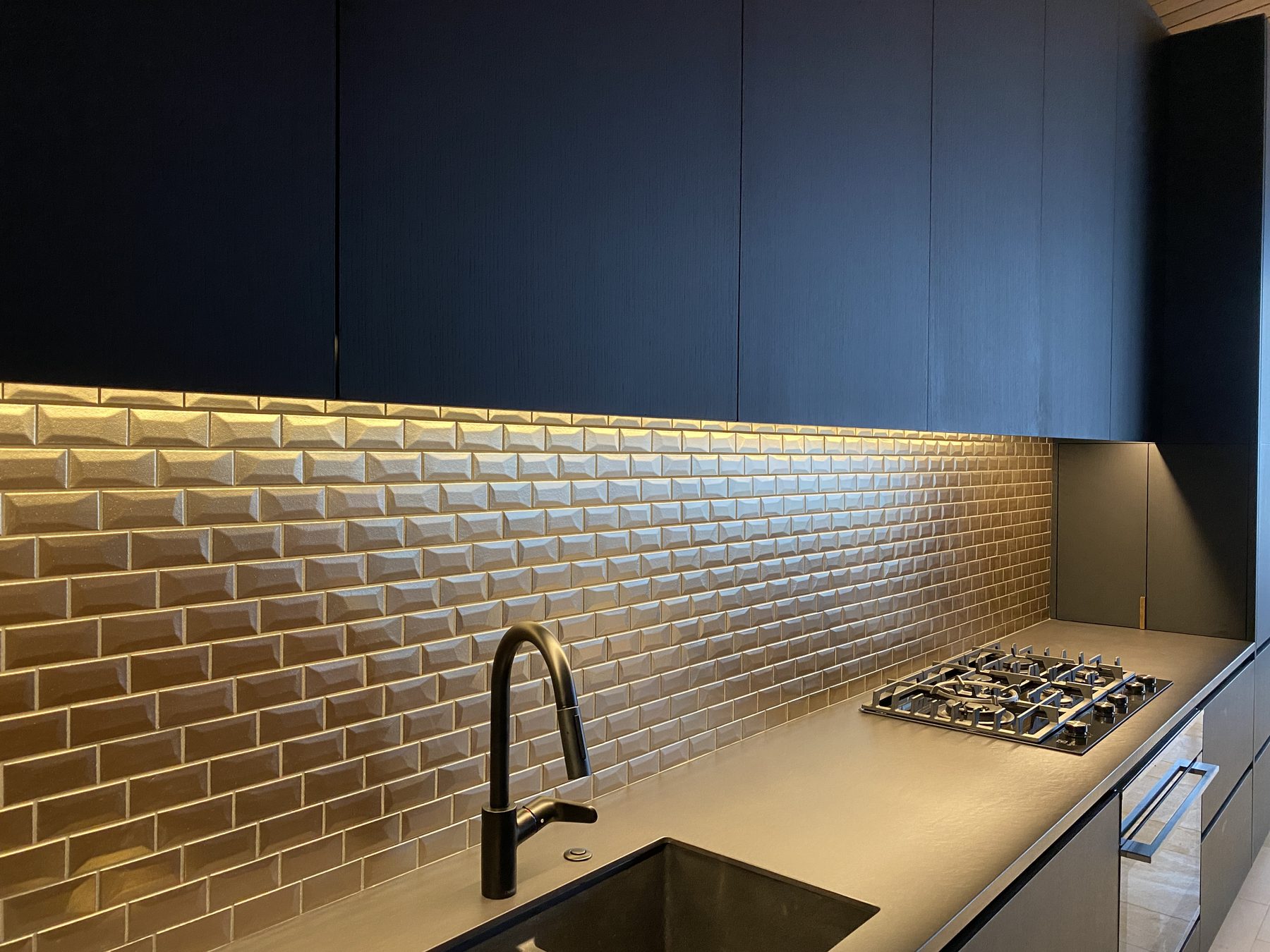 Bronze bevelled subway tile splashback in a black kitchen