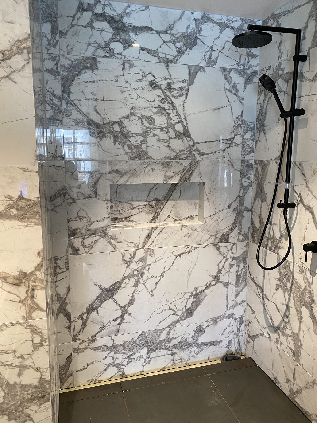 Bookmatched marble-look large format porcelain shower with recessed niche