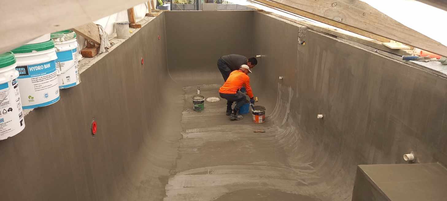 The Bespoke Tiling Solutions crew applying immersion-rated waterproofing inside a swimming pool shell